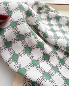 Detail of silk scarf showing green geometric hexagon pattern and H-letter chain design