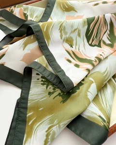 Close-up of silk scarf showing vibrant green leaf prints and smooth satin texture