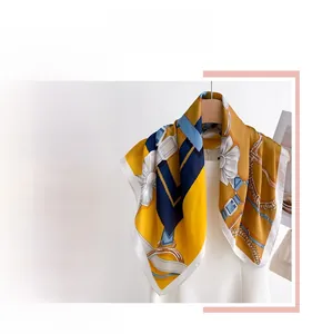 Détail d'un foulard en soie jaune avec imprimés de chaînes et motifs floraux blancs