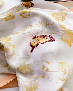 Detail of silk scarf showing yellow floral patterns and butterfly prints on cream fabric