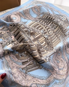 Detailed view of architecturally printed blue silk scarf draped on a luxury leather bag