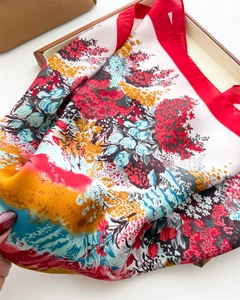 Close-up of a floral silk scarf with red edges and vibrant print on a wooden box