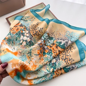 Detail of elegant floral print silk scarf with vibrant orange and cyan satin patterns