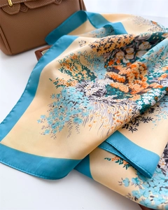 Detail of colorful floral silk scarf draped elegantly next to a brown leather handbag