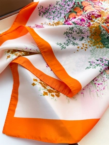 Detail of floral silk scarf with vibrant orange border and smooth satin texture