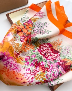 Detail of vibrant floral print silk scarf with an orange border on a display tray
