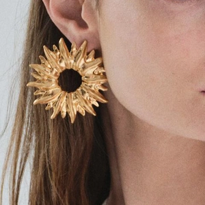 Golden sunburst flower earrings with hollow metal texture on a female model