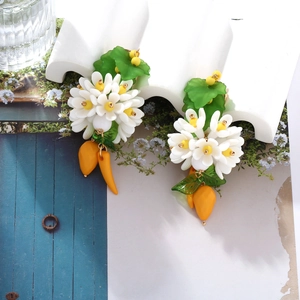 Détail de boucles d'oreilles florales avec pétales blancs, feuilles et gouttes de fruits