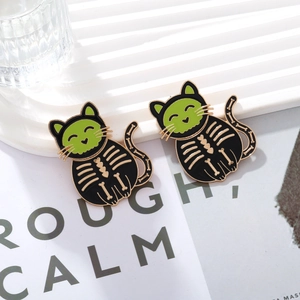 Detail of two Halloween black cat enamel pins with green faces and gold heart-shaped bone motifs