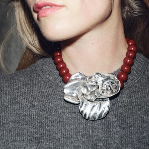 Close-up of oversized silver flower pendant with deep red resin beaded necklace on model