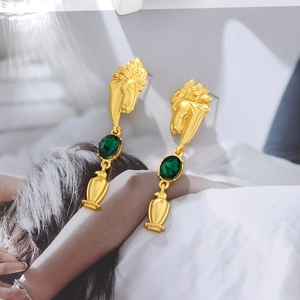 Detail of vintage gold horse head earrings with oval green glass stones and long pendants