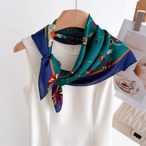 Detail showing high-end floral silk square scarf tied on a white dress with dark green leaf patterns