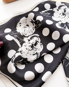 Dettaglio di un foulard in seta con pois bianchi e stampa floreale su sfondo nero