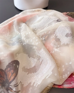 Vue macro d'un foulard en soie ivoire avec imprimé papillon orange et tissage jacquard
