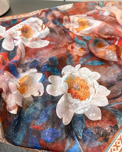 Détail d'un foulard en soie imprimé floral avec fleurs blanches sur dégradé orange et bleu