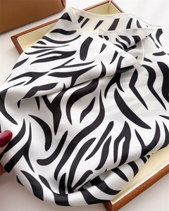 Detail view of zebra print silk scarf draped in a wooden gift box with soft lighting