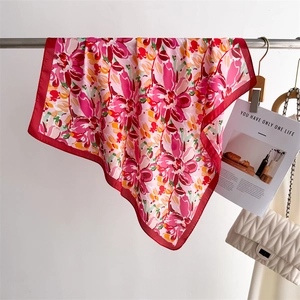 Detail of vibrant floral print silk scarf with red border hanging on metal rack