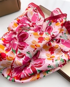 Detail of silk scarf with vibrant floral print on a tray next to a leather handbag