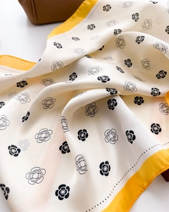 Gros plan sur foulard en soie à imprimé camélia et bordure jaune sur un sac marron