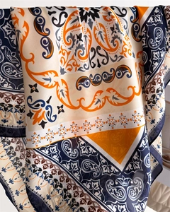 Close-up of silk scarf showing navy and orange paisley patterns with glossy satin texture
