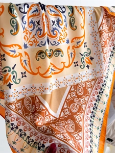 Detailed pattern of silk scarf showing orange paisley and scrollwork on cream fabric