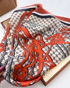 Detailed view of orange silk square scarf with equestrian motifs in a wooden tray