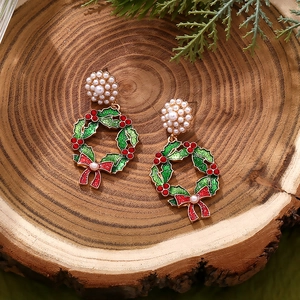 Detailed view of Christmas wreath earrings with pearls and red bows on wood background