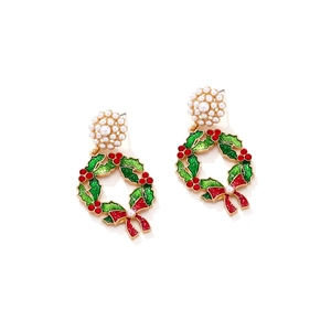 Close-up of Christmas wreath earrings with red bow and faux pearls on white backdrop