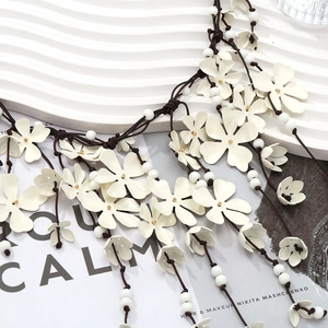 Detail of white floral cascading necklace with golden beads and woven brown cord