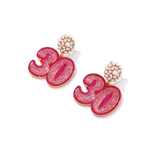 Détail de boucles d'oreilles numéro 30 pailleté rose avec monture dorée et fleurs de perles