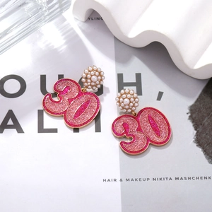 Détail de boucles d'oreilles chiffre 30 paillettes roses avec perles et bordures dorées