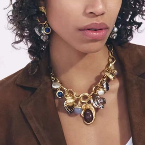 Nahaufnahme einer Vintage-Goldkette mit Herz- und Insektenanhängern an einem Model