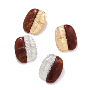 Detail of amber resin and textured geometric metal earrings with a shimmering finish