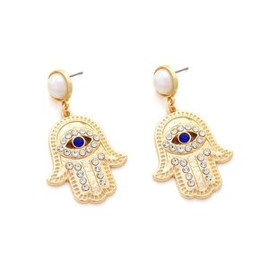 Macro detail of Hamsa Hand earrings featuring a blue evil eye and white pearl accents