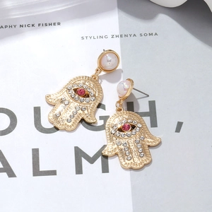 Golden Hamsa hand drop earrings with pink crystals and evil eye design on magazine