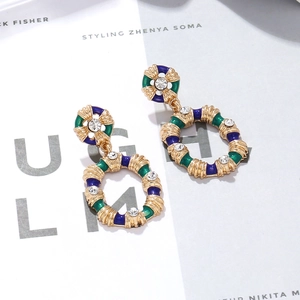 Boucles d'oreilles baroques dorées avec émail vert et bleu sur un fond de magazine chic