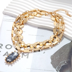 Close-up of double-layered gold chain necklace with dark gray marble oval pendant