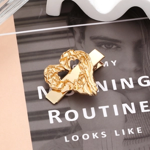 Golden heart-shaped hair clip with lava texture on a minimalist magazine background
