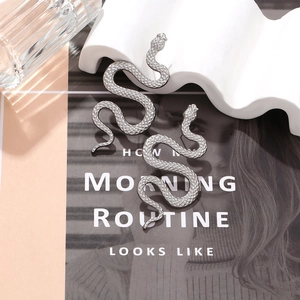 Detailed view of silver snake-shaped earrings with textured finish on a fashion magazine