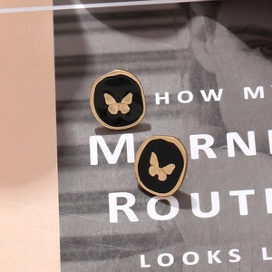 Elegant irregular black enamel butterfly stud earrings with gold accents on a magazine