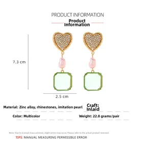 Detail view of heart-shaped earrings with faux pearl and green resin pendant, 7.3cm height