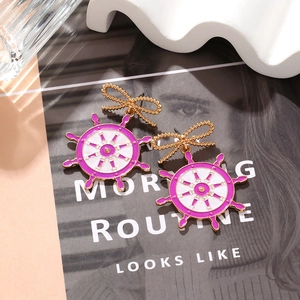 Golden ship wheel earrings with purple enamel details and a stylish bow hook design
