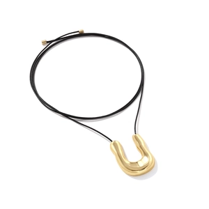 Detailed view of a polished gold U-shaped alloy pendant on a black cord necklace