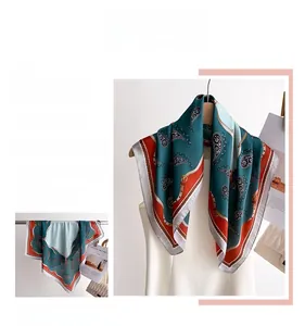 Detailed view of square silk scarf with paisley patterns in dark green and orange tones