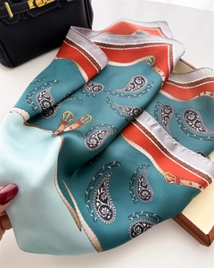 Detail of printed silk scarf featuring paisley and belt motifs held by hand
