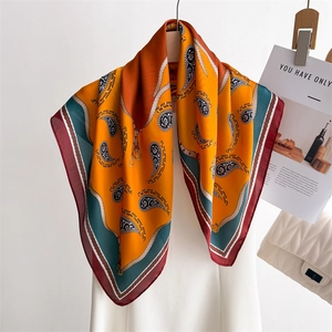 Elegant paisley silk scarf in orange and teal, styled on a wooden hanger with a white bag