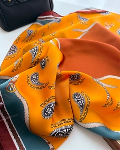 Detailed shot of silk scarf featuring orange paisley patterns and leather belt motifs