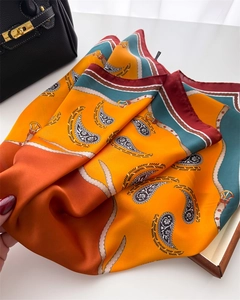 Detail of luxury silk scarf with orange paisley patterns draped on a black leather handbag