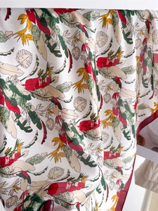 Close-up of tropical floral print silk scarf with red, green, and yellow leaf patterns