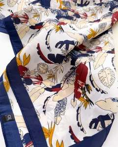 Detailed close-up of tropical floral print silk scarf with navy borders and brand label